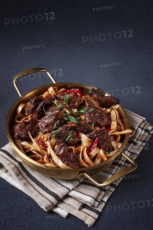 Udon noodles with Mongolian beef, green onions and vegetables, in a brass pan, on a gray background, homemade, no people