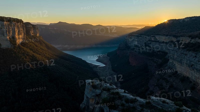 A breathtaking view of the Panta de Sau Reservoir at sunset, surrounded by steep cliffs and lush greenery. The golden light enhances the serene and natural beauty of the landscape