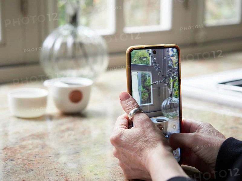 Close up view, female hands holding smartphone taking a photo of a cup on kitchen countertop. Out of focus background