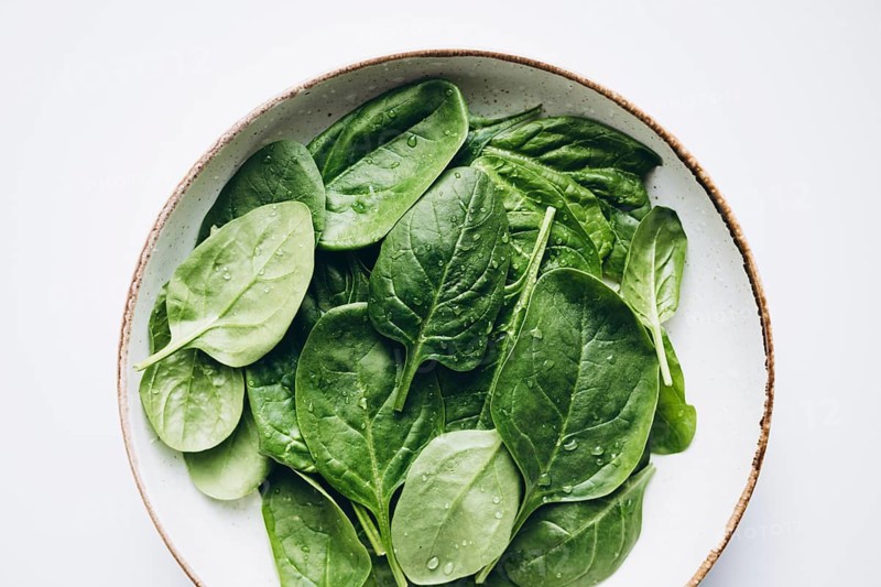 A bowl filled with fresh green spinach leaves, glistening with water droplets. Capturing their vibrant color and natural freshness, perfect for a healthy lifestyle theme