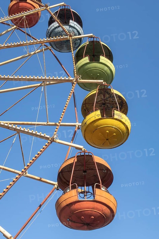 From below a vivid close-up of a Ferris wheel in Georgia with colorful gondolas against a clear blue sky, showcasing a lively amusement attraction in a sunny setting