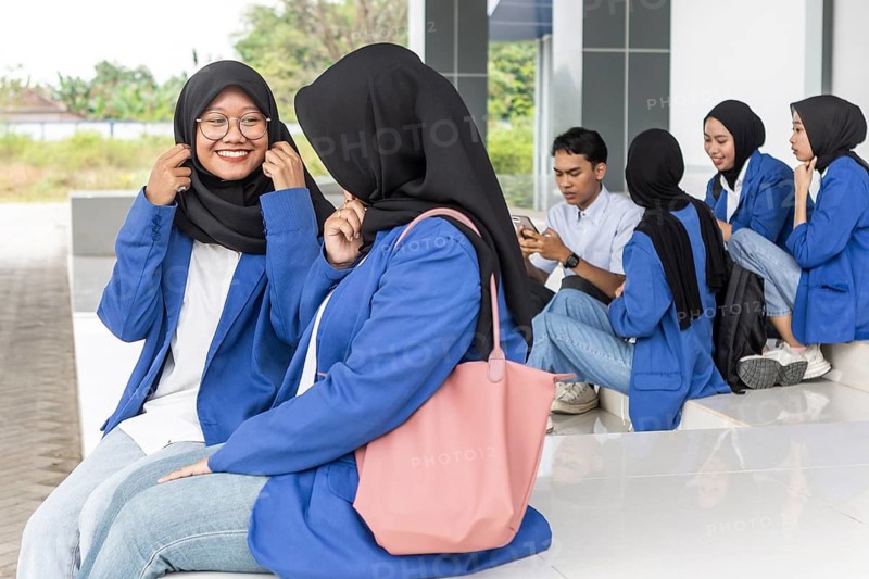 A group of Asian Muslim students socialize on a university campus in casual attire. They prepare for their return to school, wearing blue jackets and engaging in lively conversation
