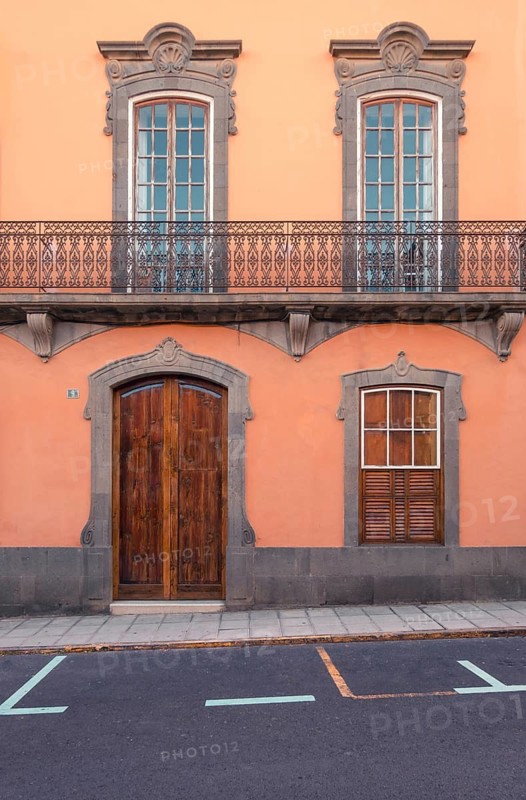 Capturing the timeless charm of Las Palmas de Gran Canaria, this image features a traditional orange building with exquisite window and balcony designs, contrasted against a gray winter sky