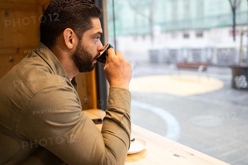 A man in a cafe enjoys a warm coffee, gazing outside on a rainy day in the city. The serene atmosphere captures a moment of solitude and relaxation in a cozy setting