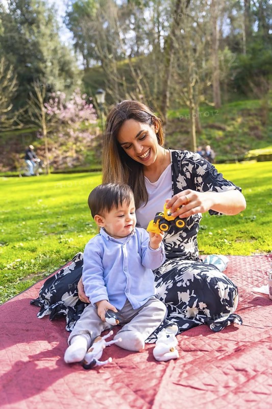 Mother and baby boy enjoying quality time together, playing with a toy truck on a blanket in a sunny park