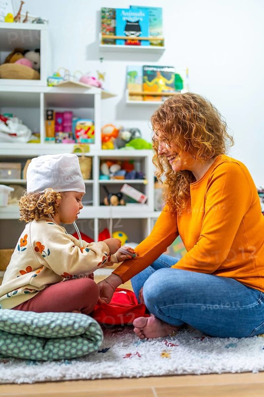 Vertical photo of a cute girl and mother playing nurses sitting on the floor at home
