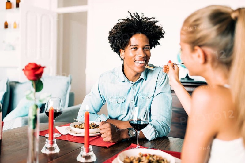 A couple enjoys a romantic dinner at home, featuring candles and wine. The scene is intimate and warm, with a focus on the shared dining experience and atmosphere