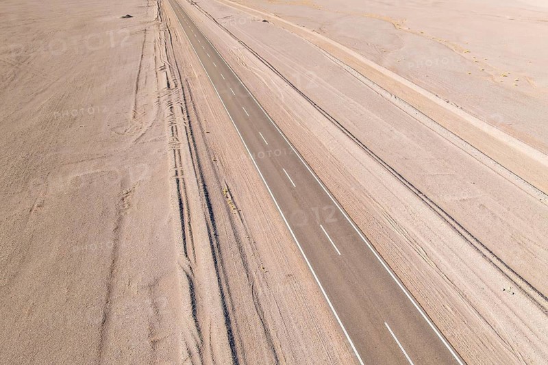 Aerial view of a long, straight road cutting through a vast, barren desert landscape in the argentine Puna, emphasizing isolation and tranquility in the open wilderness