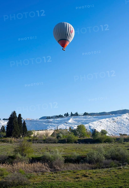 A hot air balloon floats over green countryside and white limestone terraces, sinter terraces, lime sinter terraces, travertine terraces, Pamukkale, Denizli, UNESCO World Heritage Sites, Anatolia, Turkey