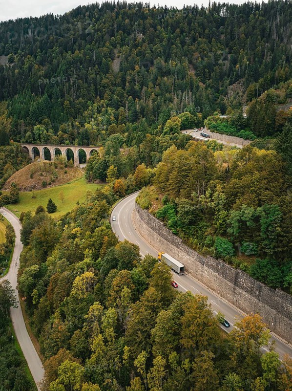 Aerial view of a winding mountain road lined with lush forest and a railway bridge in a hilly landscape, Ravenna Gorge, Black Forest, Germany