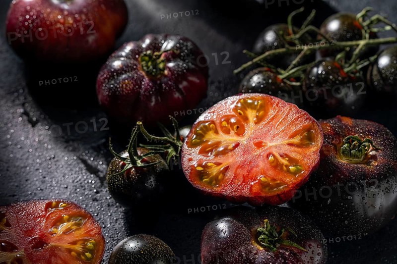 A collection of ripe heirloom tomatoes with rich colors, glistening with water droplets on a dark background. The vibrant textures and earthy tones create a rustic ambiance