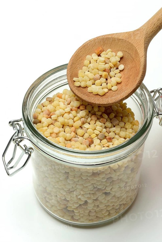 Fregola in wooden spoon and glass container, pasta variety from Sardinia, Italy