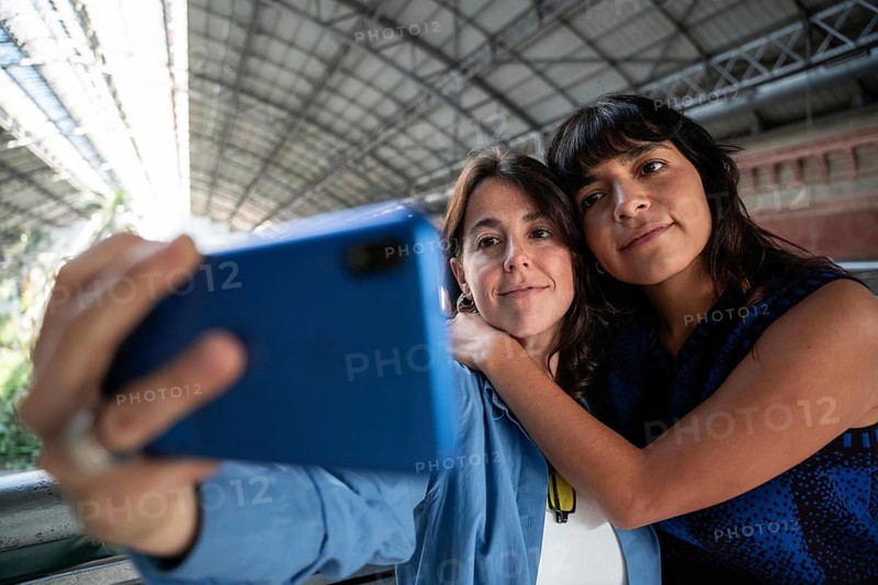 A close-up image of a multiethnic lesbian couple capturing a selfie together. Their joyous expressions and embrace celebrate diversity and love. Perfect for LGBTQIA+ themes