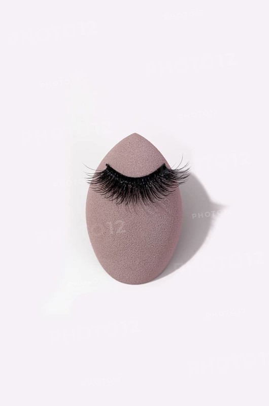 False eyelashes gracefully rests on a makeup sponge. The white background highlights the contrast, emphasizing the lush texture and elegant curve of the lashes