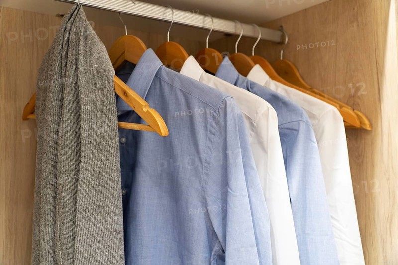 A selection of blue and white shirts, hangs neatly on wooden hangers in a wooden closet. The scene exudes organization and style in a home interior