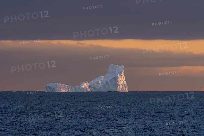 Iceberg in the open sea at sunset, warm light on ice structures, dark cloud cover on the horizon, South Atlantic, near South Georgia