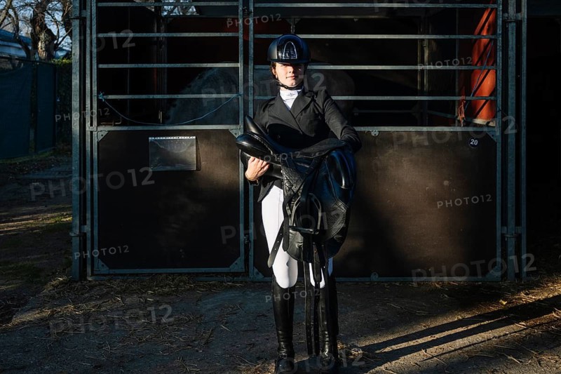 Equestrian preparing for a dressage event, holding a saddle outside a stable Dressed in formal equestrian attire, emphasizing the elegance and precision of classical dressage