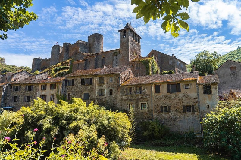 A picturesque Chateau brousse castle medieval rises above a charming village in france, nestled in lush greenery under a vibrant blue sky