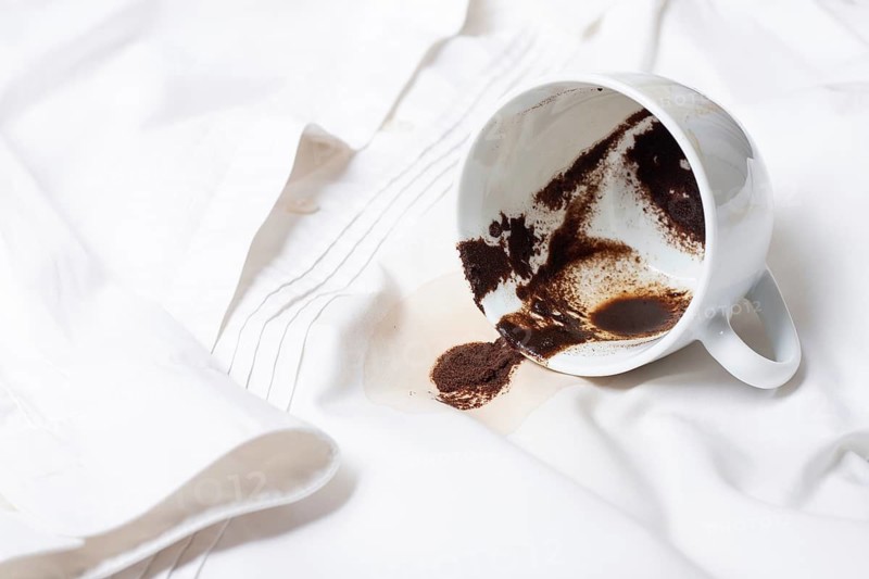 A white cup with the remains of coffee, spilled, lies on a white shirt, there are no people, a soft focus