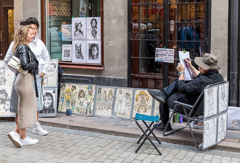 Young couple having a portrait taken by a street draftsman, Västerlånggatan in the old town of Gamla Stan, Stockholm, Sweden