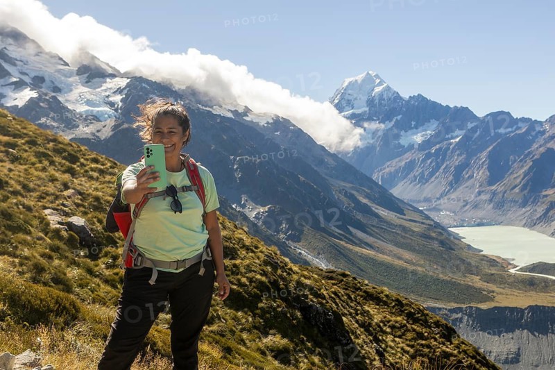 A woman enjoying the beauty of autumn on Mount Cook, New Zealand, captures a selfie amidst stunning mountain views, showcasing nature vibrant autumnal hues
