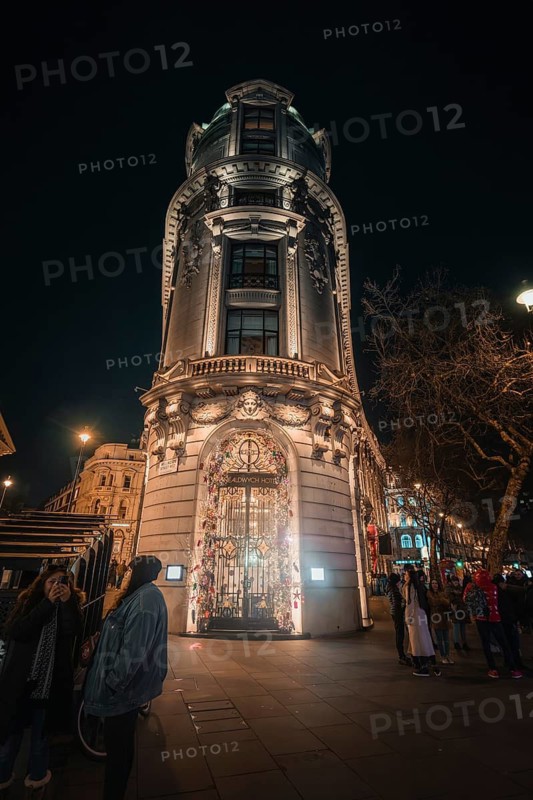 An illuminated, historic building in the city at night, passers-by pass by, New Year's Eve London, United Kingdom