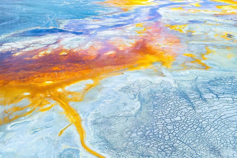 This image captures a stunning aerial view of a multicolor abstract landscape, showcasing vibrant oranges, blues, and yellows mixed with intricate patterns