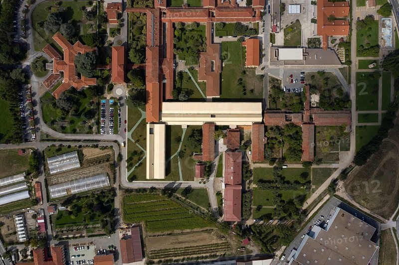 Aerial view of a large hospital with interconnected buildings surrounded by greenery, roads, and parking lots. The orderly design creates a harmonious urban landscape