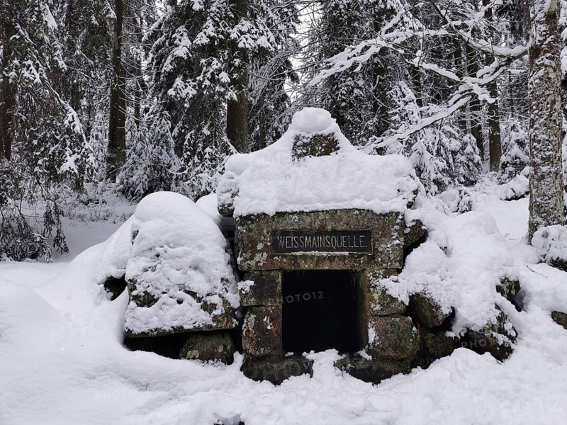 Fountain and spring of the White Main, snow-covered stone monument in the forest, surrounded by peace and cold in a wintry atmosphere, Weissmainsquelle, hiking in the Franconian Forest nature park Park