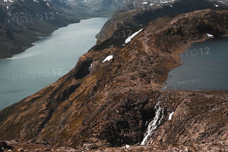 A breathtaking view of a cascading waterfall flowing into a mountain lake in Norway Surrounded by rugged terrain and a serene valley, the scene captures nature's raw beauty