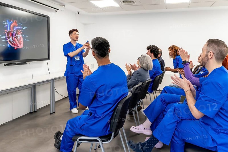 Medical student delivering a presentation about human heart anatomy to a diverse group of healthcare students and professionals applauding in a bright classroom setting