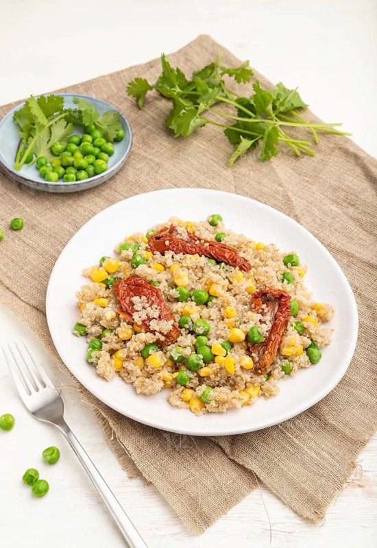 Quinoa porridge with green pea, corn and dried tomatoes on ceramic plate on a white wooden background and linen textile. Side view, close up