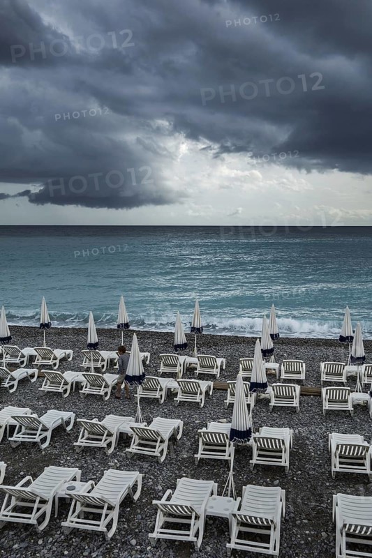 White reclining chairs on deserted beach during bad weather with dark, menacing rain clouds over the sea