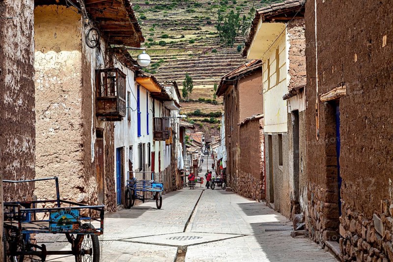 A narrow street with traditional houses and Andes in the background, the city of Ollantaytambo in the Andes of Peru