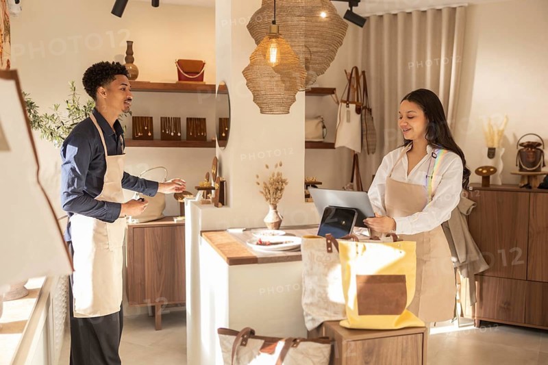 Two staff member converse in a stylish bag store. The store interior showcases a variety of bags, creating a welcoming shopping environment with natural lighting