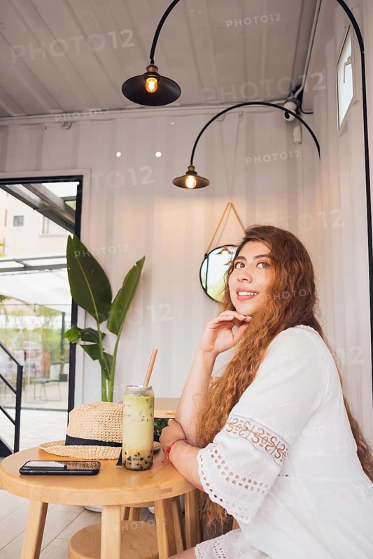A young American Latin woman sits at a stylish cafe table, enjoying a refreshing drink. She exudes a relaxed and joyful lifestyle, embodying modern elegance