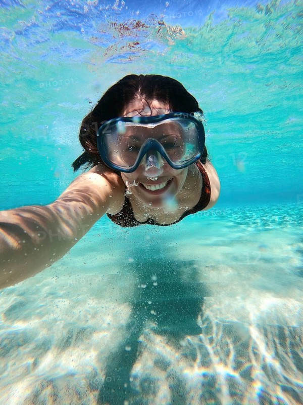 A woman enjoys snorkeling in the crystal-clear waters off the Greek coast. Her smile is visible through the snorkel mask as she captures the vibrant underwater experience