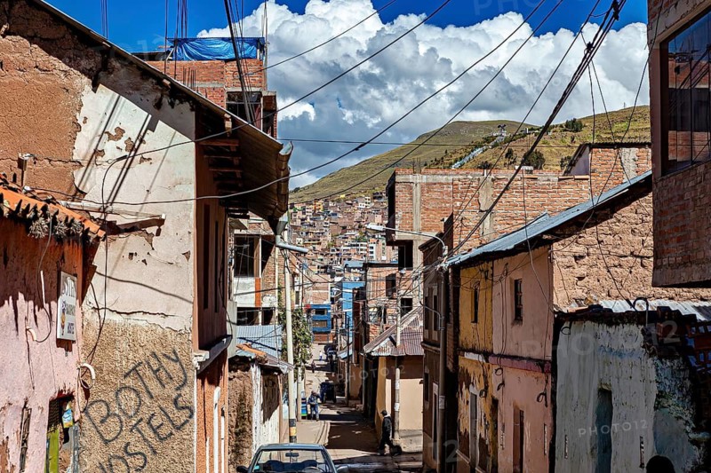 Narrow street with brick and plaster houses surrounded by mountains under blue sky with clouds, The roads and houses of Puno in Peru