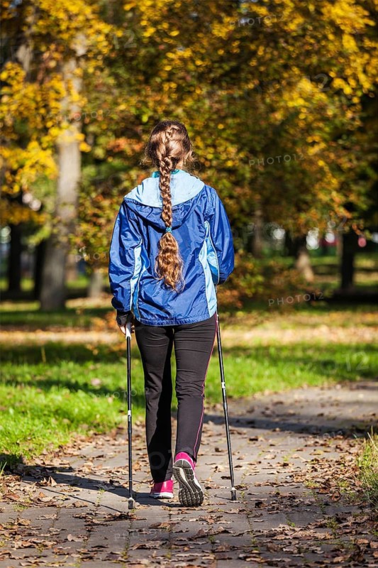Nordic walking adventure and exercising concept, woman hiking withnordic walking poles in park
