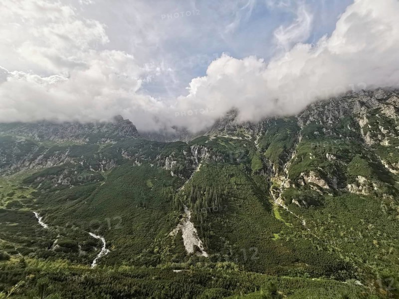 Wide view of lush mountain landscape with green valleys and dramatic clouds covering the peaks, Zakopane, hiking in the High Tatras National Park, Carpathian Mountains, Poland