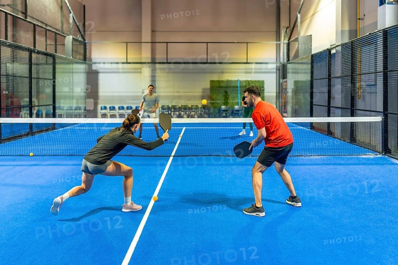 Four active individuals enjoying a friendly doubles pickleball match on a vibrant blue indoor court, focusing on skill, strategy, and teamwork during a dynamic game