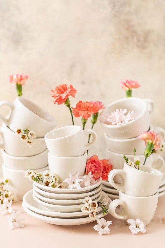 Set of white cups, plates, and saucers beautifully decorated with fresh pink and white spring flowers, providing a soft, aesthetic look against a creamy background