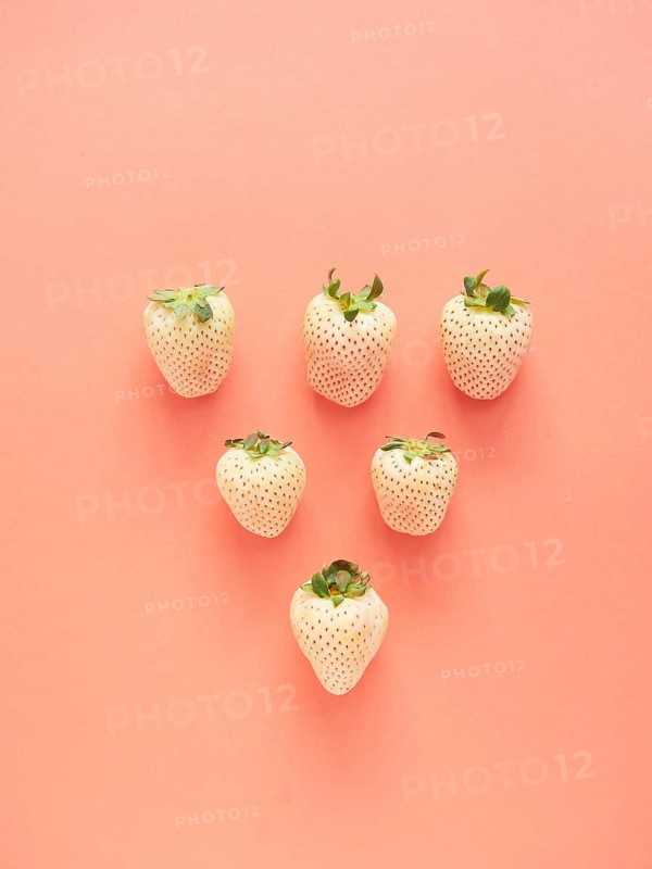 White strawberries arranged in a row forming a triangle on a pink background. top view with copy space