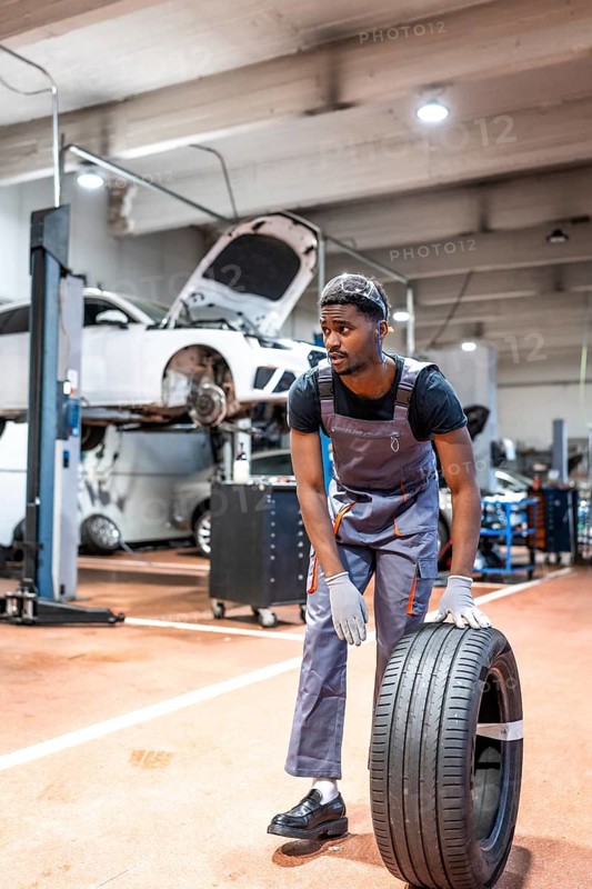 Young mechanic lifting a car tire in a professional workshop, demonstrating expertise and dedication to vehicle maintenance