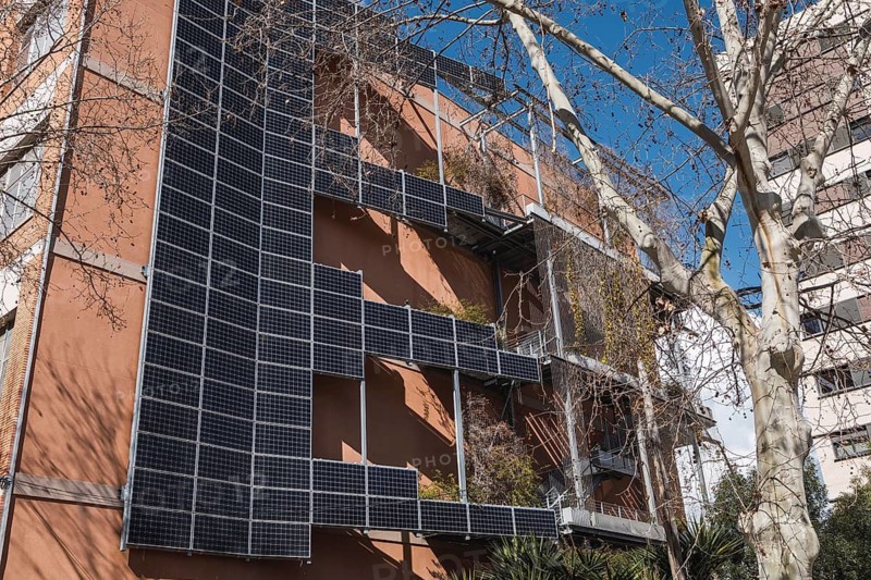 Solar panels cover the facade of a modern urban building, promoting sustainable energy. The architecture integrates greenery, enhancing eco friendly urban lifestyle