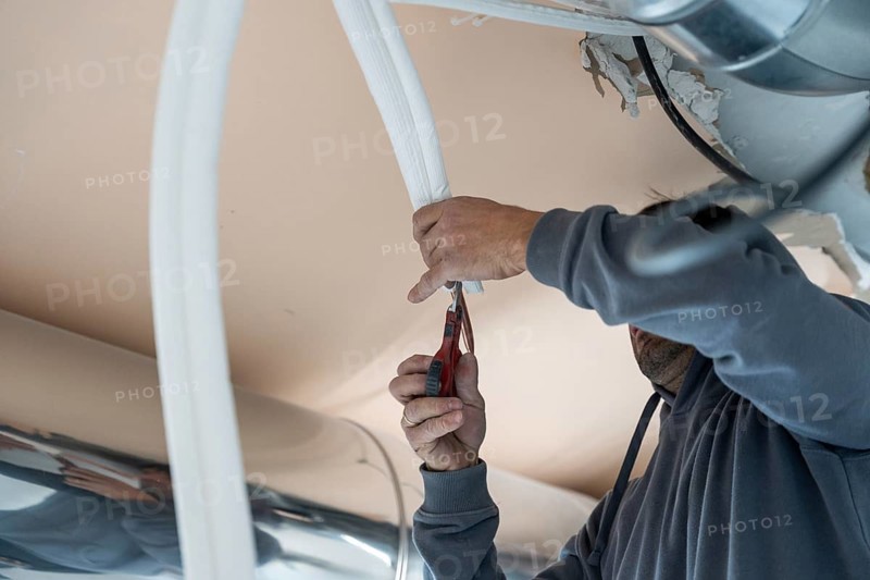 Hvac technician cutting insulation for an air conditioning duct, carefully trimming material for a precise fit during installation and maintenance inside a commercial building