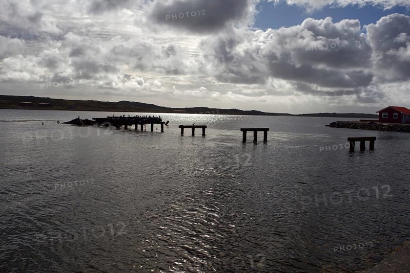 Abandoned and half-destroyed pier structures under a cloudy sky, near a small red hut on the shore, Stanley, East Falkland, Falkland Islands (UK), British Overseas Territory