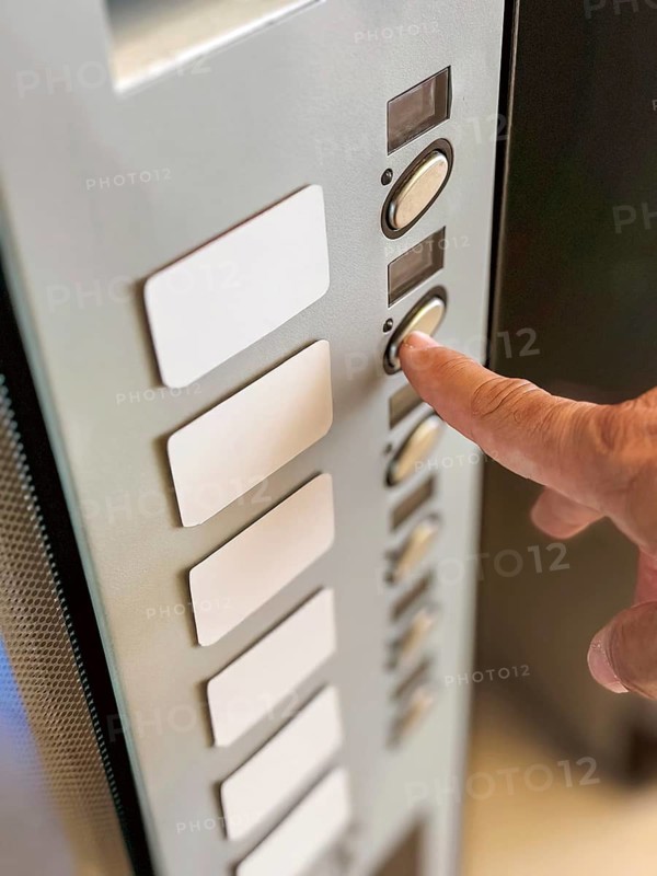 A close-up view of a person's hand pressing a button on an elevator panel. The panel features several buttons arranged vertically, highlighting a modern indoor access system