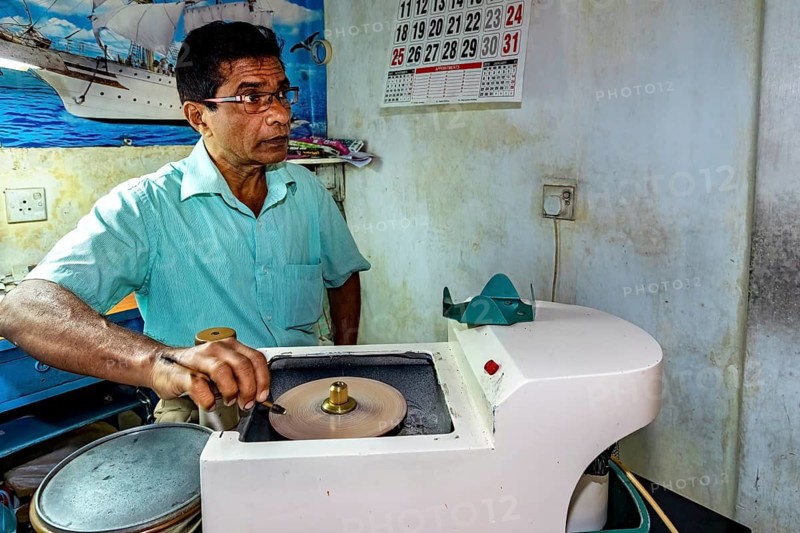 Man working with a machine in a room with a maritime poster on the wall, The gemstone cutters in the city of Ratnapura in Sri Lanka