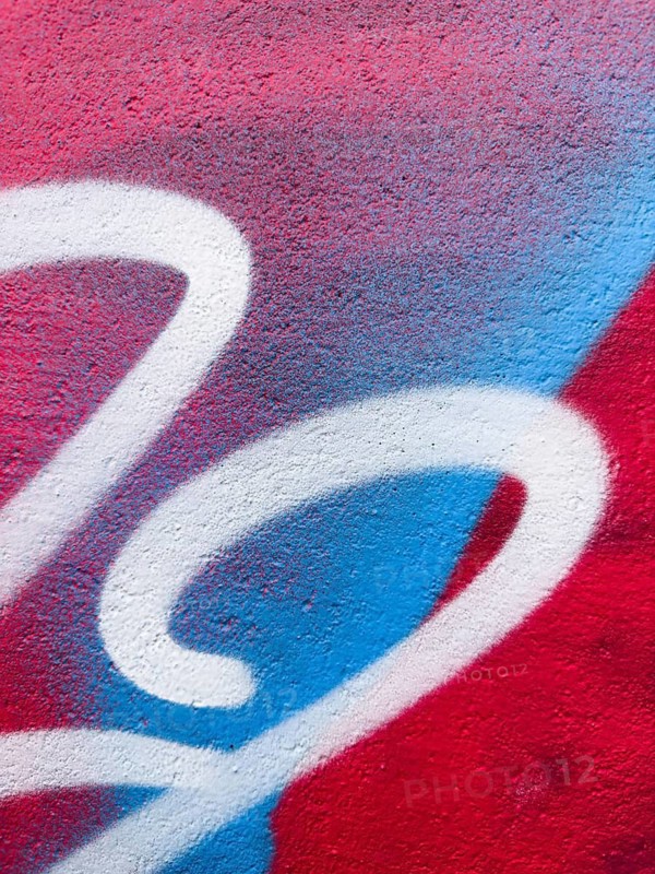 A close-up of vibrant graffiti artwork, showcasing red, blue, and white colors on a textured wall. The abstract, curving shapes and bold contrasts create a dynamic, urban feel. Perfect for backgrounds or modern art themes